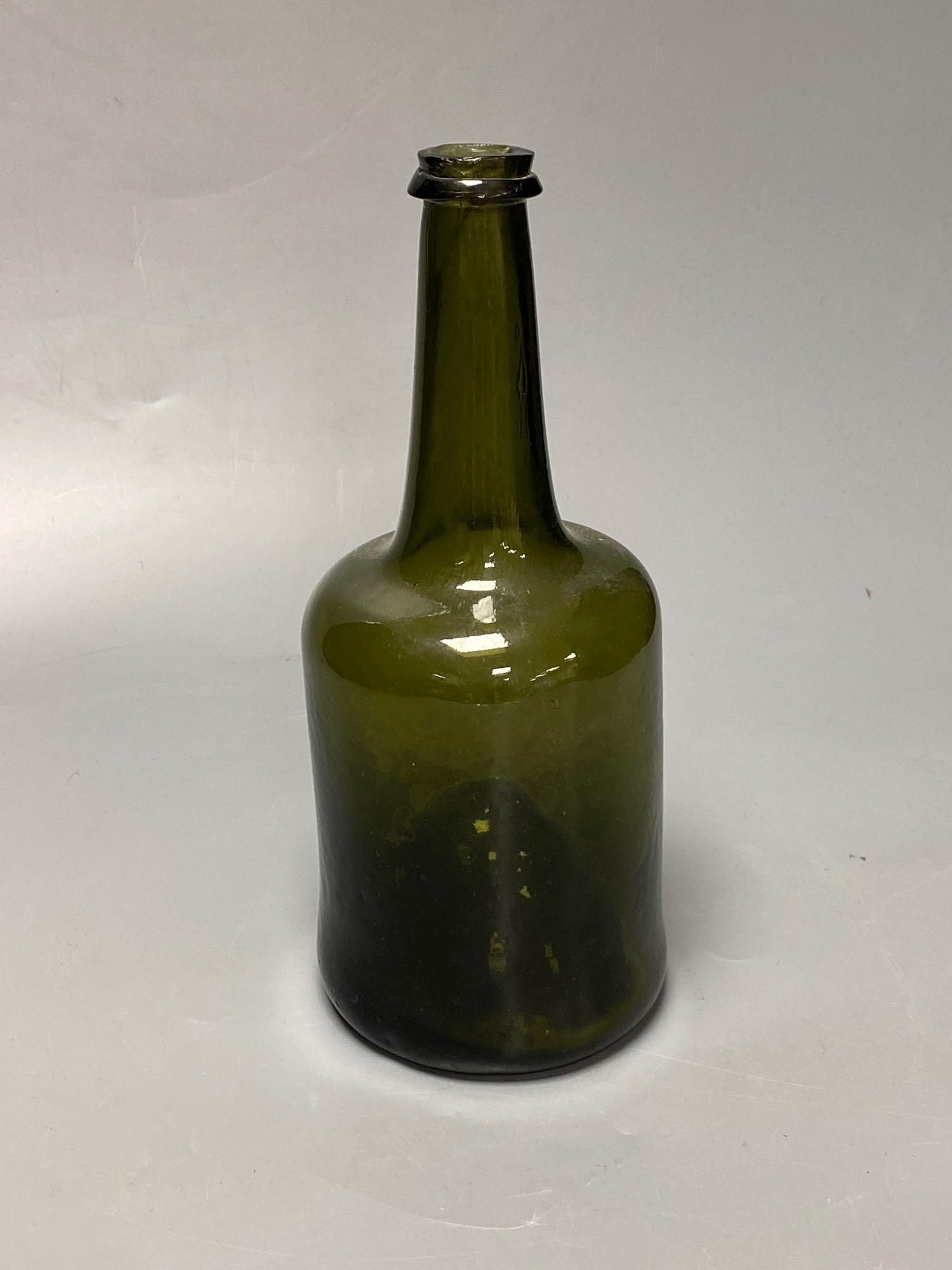 An early 18th century dark green glass wine bottle with a kick in based, 23cm